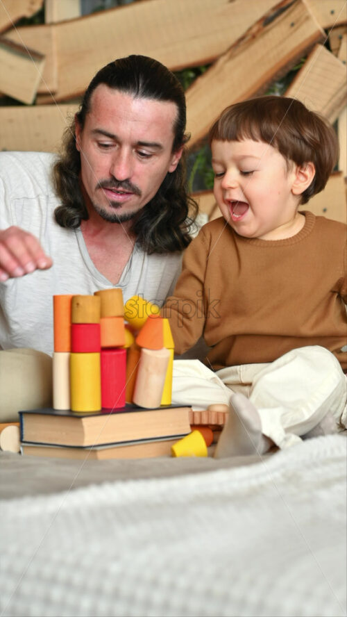 Video - Father playing with his son with colourful, ecological wooden toys on the bed
