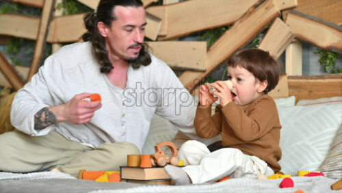 Video - Father playing with his son with colourful, ecological wooden toys on the bed