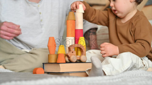 Video - Father playing with his son with colourful, ecological wooden toys on the bed