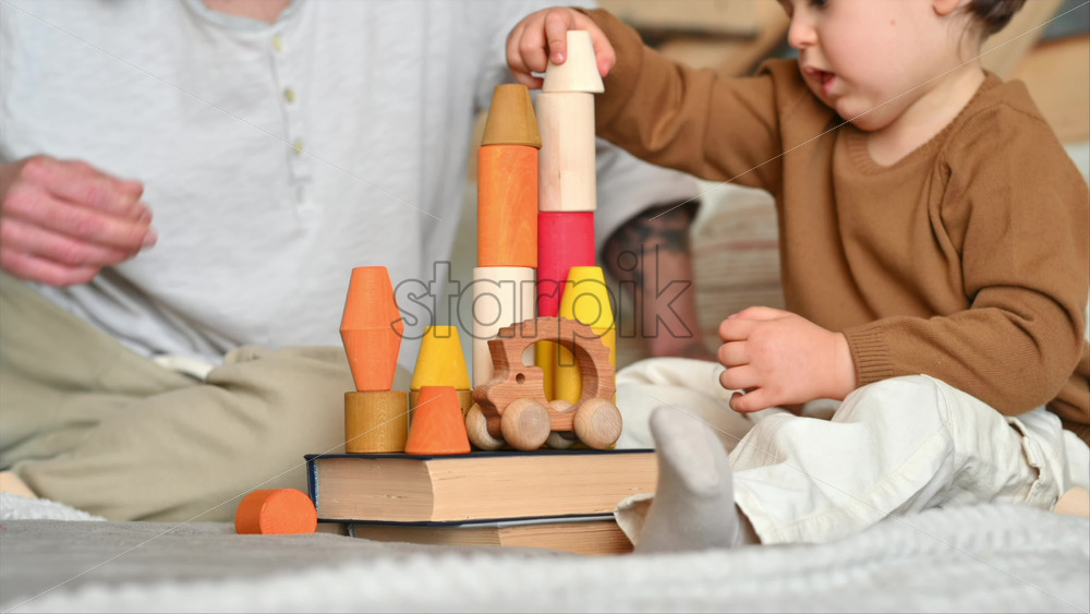 Video - Father playing with his son with colourful, ecological wooden toys on the bed