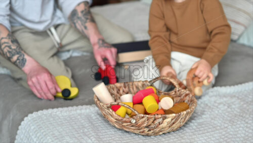 Video - Father playing with his son with colourful, ecological wooden toys from a basket on the bed