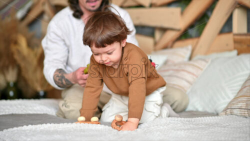Video - Father playing with his son with colourful, ecological wooden toys on the bed