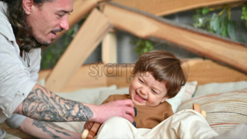 Video - Father playing with his son with colourful, ecological wooden toys on the bed