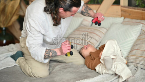 Video - Father playing with his son with colourful, ecological wooden toys on the bed