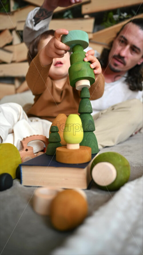 Video - Father playing with his son with colourful, ecological wooden toys on the bed. Vertical