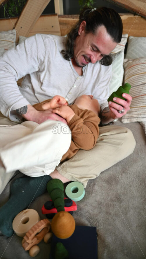 Video - Father playing with his son with colourful, ecological wooden toys on the bed. Vertical