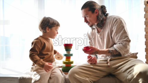 Video - Father playing with his son with colourful, ecological wooden toys near a window