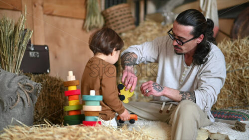 Video - Father playing with his son with colourful, ecological wooden toys in a barn, near square hay bales
