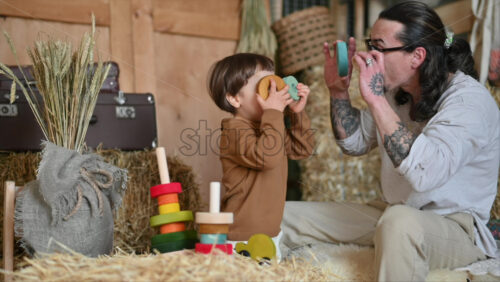 Video - Father playing with his son with colourful, ecological wooden toys in a barn, near square hay bales
