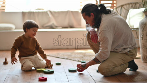 Video - Father playing with his son with colourful, ecological wooden toys on the floor, near a window