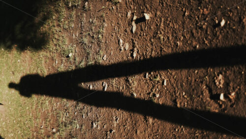 Video - Long human shadow stretching on earthy ground during golden hour. Vertical