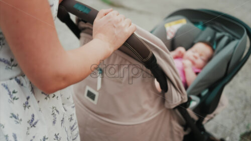 Video - Woman in floral dress pushing a baby stroller outdoors