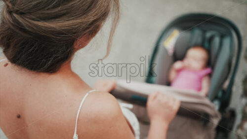 Video - Woman in floral dress pushing a baby stroller outdoors