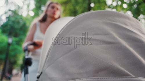 Video - Young woman walking in the park with a baby stroller on a sunny day
