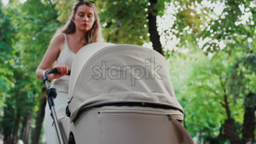 Video - Young woman walking in the park with a baby stroller on a sunny day