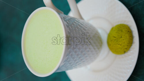 Video - Close up of a smooth matcha latte with vibrant green foam in a white cup. Vertical