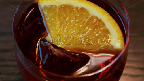 Video - Close up of a Negroni cocktail with orange slice and ice cubes on a wooden table