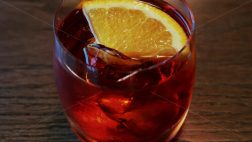Video - Close up of a Negroni cocktail with orange slice and ice cubes on a wooden table