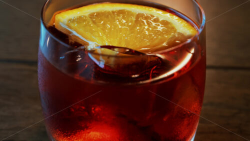 Video - Close up of a Negroni cocktail with orange slice and ice cubes on a wooden table