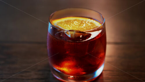 Video - Close up of a Negroni cocktail with orange slice and ice cubes on a wooden table