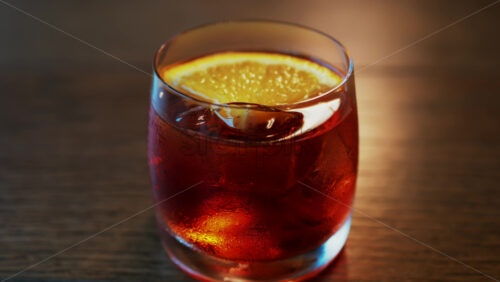 Video - Close up of a Negroni cocktail with orange slice and ice cubes on a wooden table