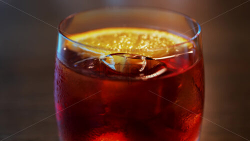 Video - Close up of a Negroni cocktail with orange slice and ice cubes on a wooden table