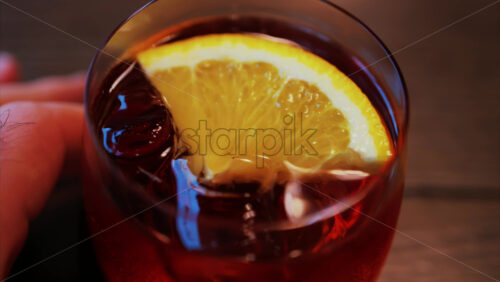 Video - Close up of a Negroni cocktail with orange slice and ice cubes on a wooden table