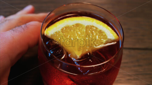 Video - Close up of a Negroni cocktail with orange slice and ice cubes on a wooden table