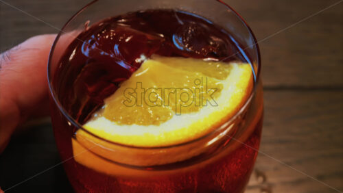 Video - Close up of a Negroni cocktail with orange slice and ice cubes on a wooden table