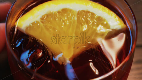 Video - Close up of a Negroni cocktail with orange slice and ice cubes on a wooden table