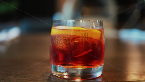 Video - Close up of a Negroni cocktail with orange slice and ice cubes on a wooden table