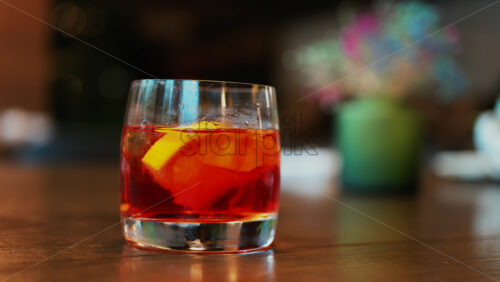 Video - Close up of a Negroni cocktail with orange slice and ice cubes on a wooden table