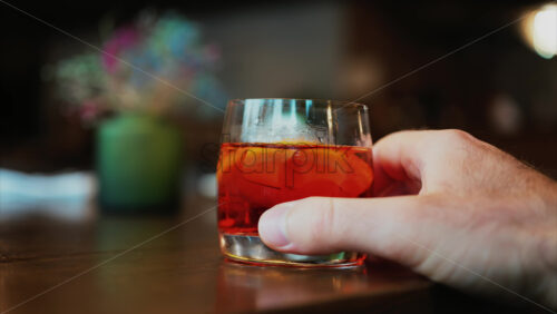 Video - Man's hand holding a glass of Negroni cocktail on a bar counter