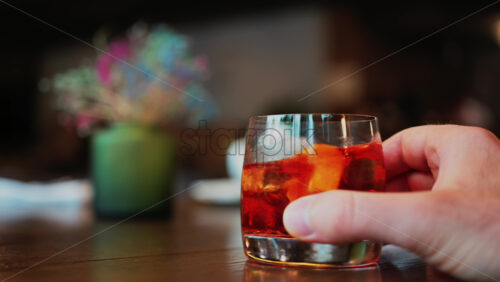 Video - Man's hand holding a glass of Negroni cocktail on a bar counter
