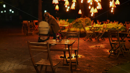 Video - A cozy outdoor cafe at night with glowing warm lights and wooden chairs glistening after rain