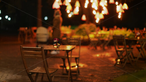 Video - A cozy outdoor cafe at night with glowing warm lights and wooden chairs glistening after rain