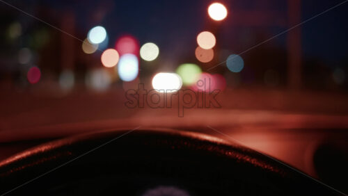 Video - Out of focus city lights seen through a car windshield at night, with the steering wheel in foreground