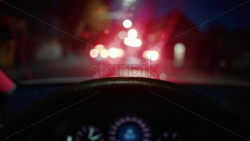 Video - Out of focus city lights seen through a car windshield at night, with the steering wheel in foreground