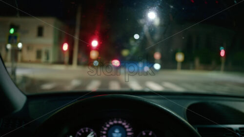 Video - Blurred view of city intersection at night, seen through a car windshield with red traffic lights glowing