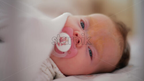 Video - Soft lit close up of a baby with a pacifier resting under a white blanket