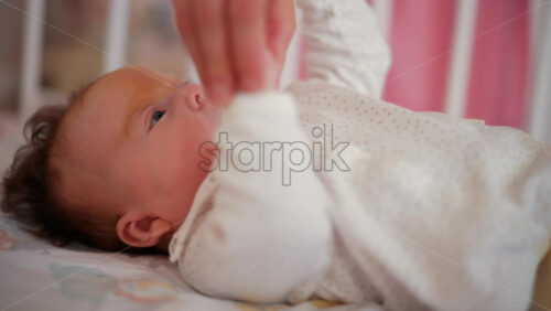 Video - A newborn baby in soft pajamas moves gently in a crib, stretching tiny hands in natural morning light