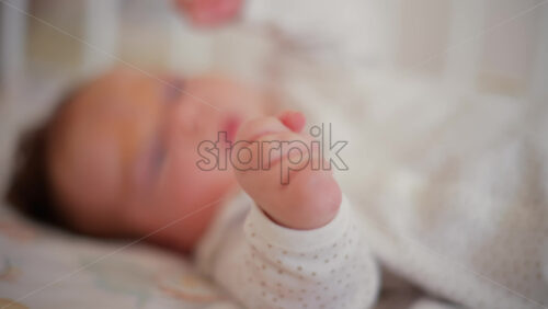 Video - A newborn baby in soft pajamas moves gently in a crib, stretching tiny hands in natural morning light