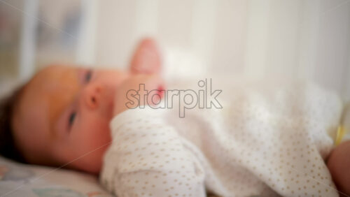 Video - A newborn baby in soft pajamas moves gently in a crib, stretching tiny hands in natural morning light