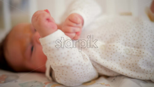 Video - A newborn baby in soft pajamas moves gently in a crib, stretching tiny hands in natural morning light
