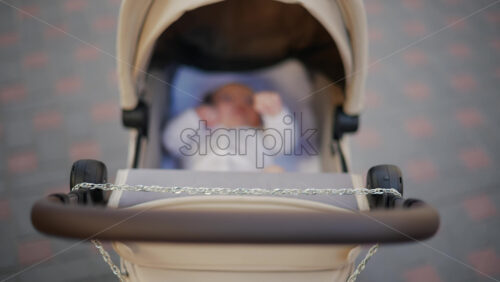 Video - Infant lying calmly in a beige stroller during a sunny walk on a paved street