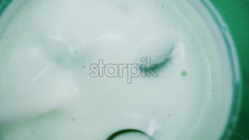 Video - Close up of a white liquid being stirred in a glass with ice