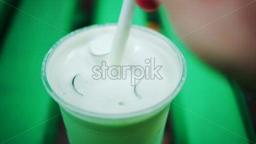 Video - Close up of an iced matcha being stirred in a glass on a green park bench