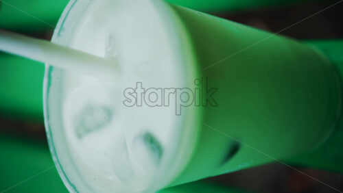Video - Close up of an iced matcha being stirred in a glass on a green park bench. Vertical