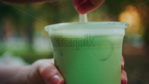 Video - Close up of woman's hand holding an iced matcha latte outdoors