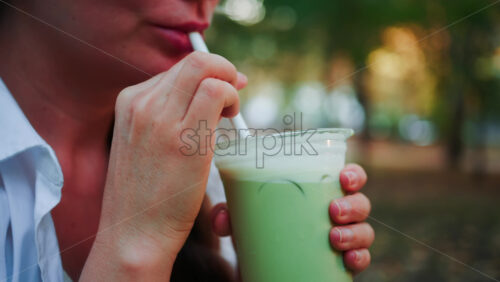 Video - Stylish young woman sipping an iced matcha outdoors, in a park